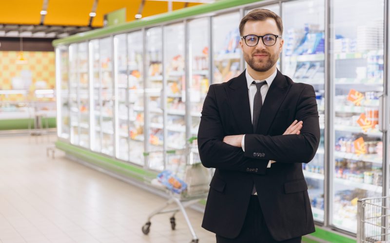 Confident supermarket manager standing with arms crossed near refrigerated shelves Supermarket manager standing with arms crossed near refrigerated shelves, smiling and looking confident
