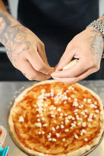 Cook in apron putting finishing touches on pizza Cropped shot of skilled chef hands putting bits of mozzarella on top of pizza
